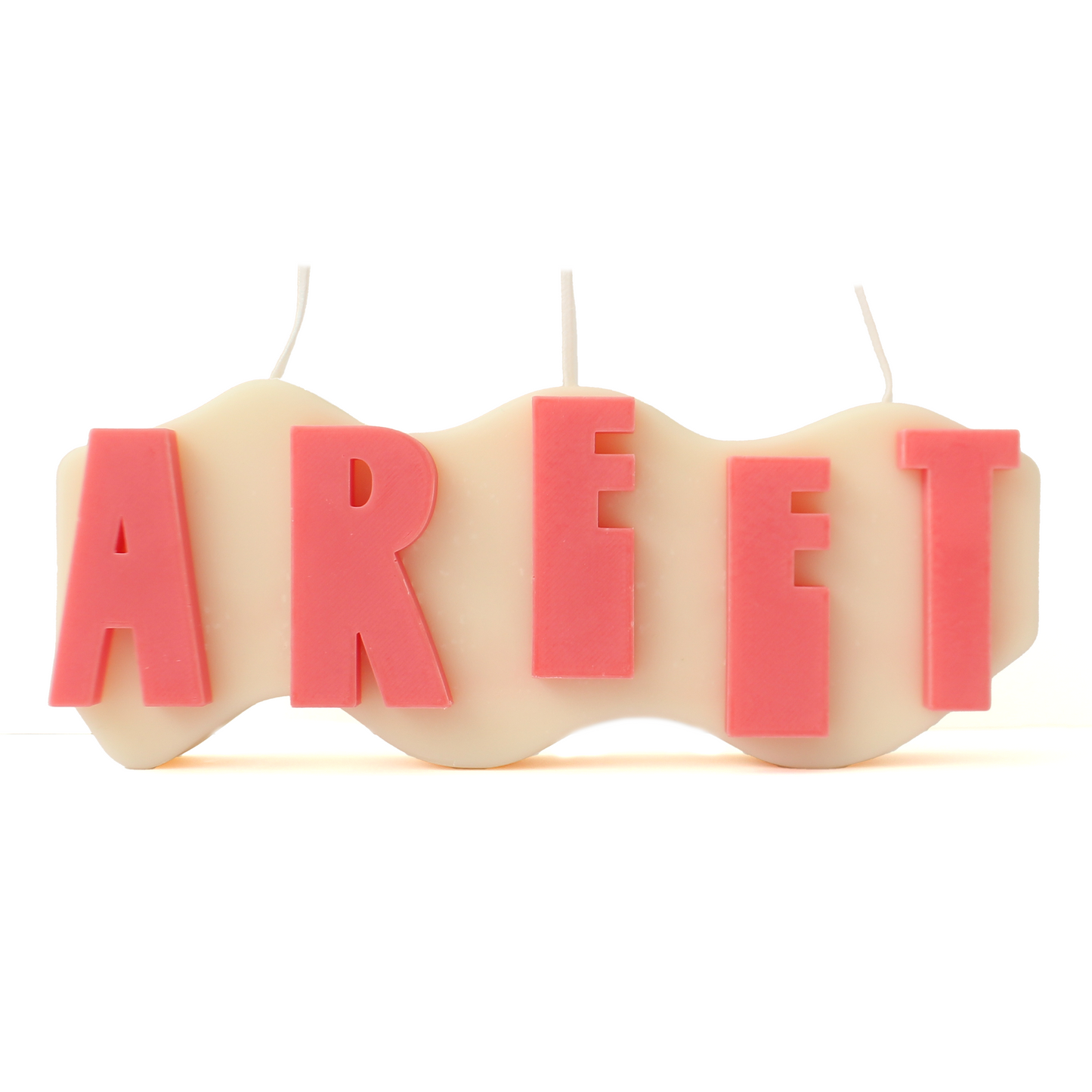 A decorative candle with a wavey body and protruding text. Measuring 17cm long and 7cm high. The body of the candle is white with pink raised letters spelling AREET from left to right. It has three wicks spread across the top of the body evenly.