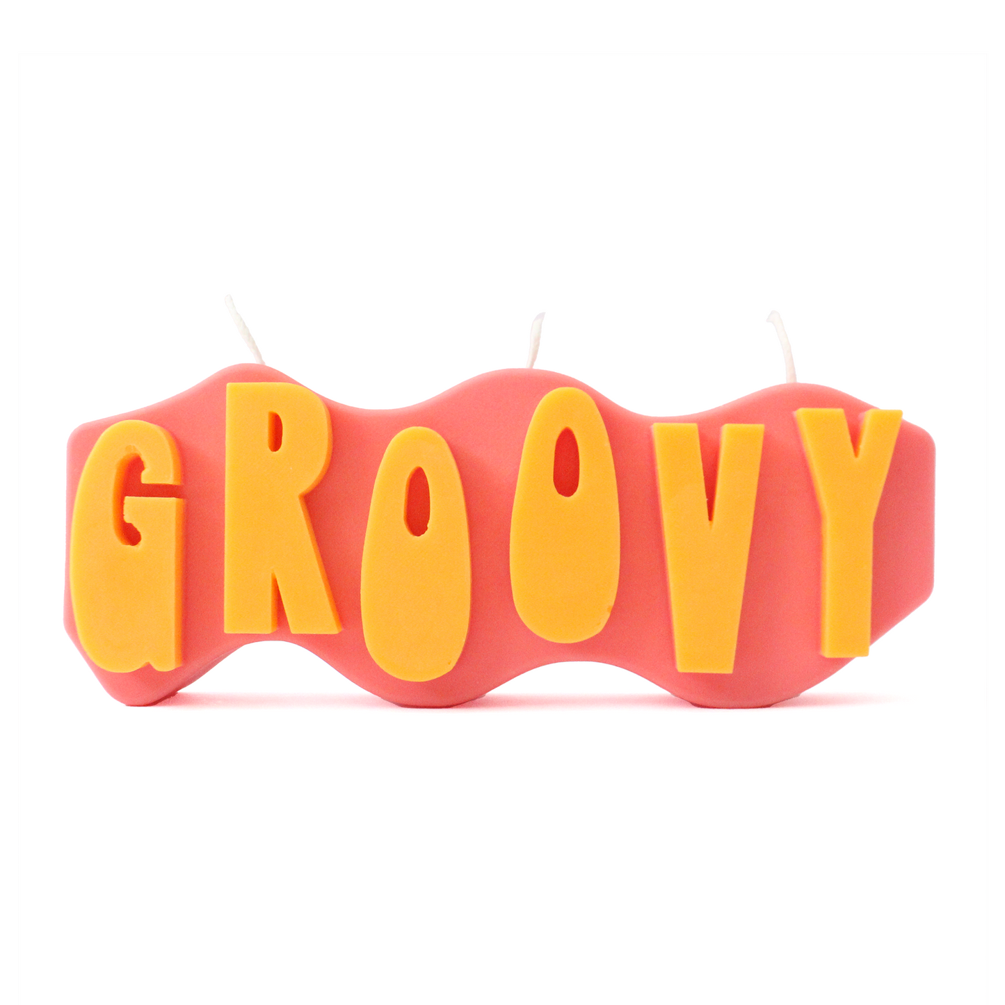 A decorative candle with a wavey body and protruding text. Measuring 17cm long and 7cm high. The body of the candle is coral pink with orange raised letters spelling GROOVY from left to right. It has three wicks spread across the top of the body evenly.