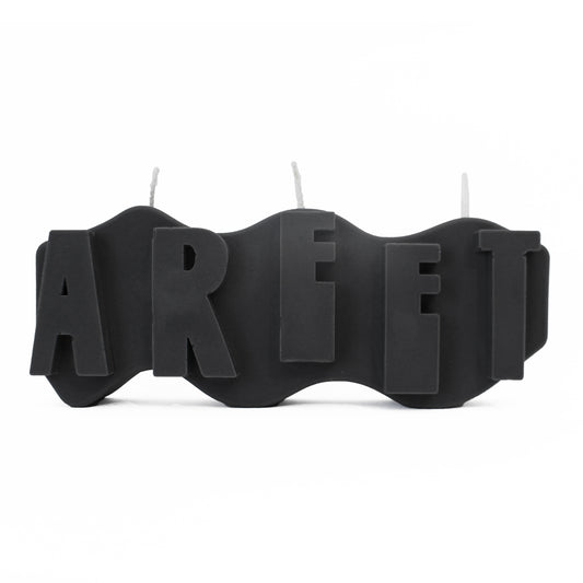 A decorative candle with a wavey body and protruding text. Measuring 17cm long and 7cm high. The  candle is charcoal black with raised letters spelling AREET from left to right. It has three wicks spread across the top of the body evenly.