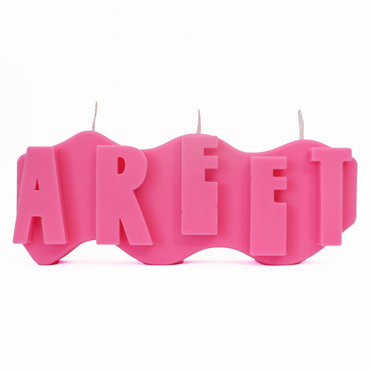 A decorative candle with a wavey body and protruding text. Measuring 17cm long and 7cm high. The candle is neon pink with raised letters spelling AREET from left to right. It has three wicks spread across the top of the body evenly. 